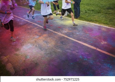 Abstract photo of a group of runners running in a color run race event. No faces visible on the legs and the feet and shoes of the runner. Lots of colorful clouds of chalk in the air and on the street
