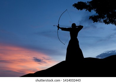 Abstract Photo Of Man Silhouette Demonstrating Martial Arts With Bow In Front Of Sunset Sky