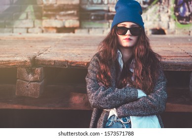 Abstract portrait of beautiful modern hipster fashionable urban young teen girl with cool attitude sunglasses and hat arms crossed enjoying a sunny day