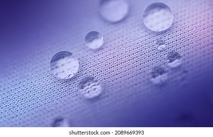 Abstract Purple Background In Trending Color Very Peri. Close-up Water Droplets Roll Off The Blue Textured Fabric, Neon Beams Illuminate The Water. Macro Photography.