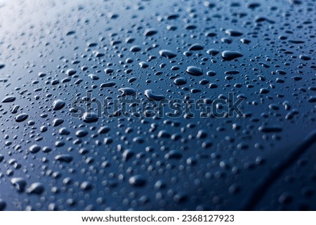 Abstract rain or water drops different size on a blue car hood surface with shiny reflections. Water droplets on dark iron surface and texture. Background and water texture for design