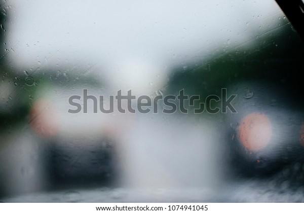 Abstract raining day, rain drops\
on the car window with traffic light, traffic is\
Background.