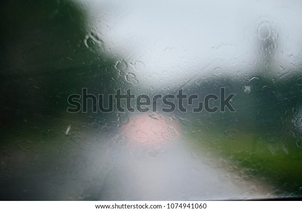Abstract raining day , rain drops\
on the car window with traffic light , traffic is\
Background