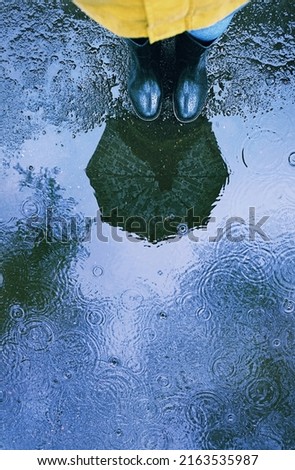 abstract rainy autumn background. reflection umbrella and rubber boots in puddle. wet asphalt road outdoor. rainy weather season. summer or autumn day.
