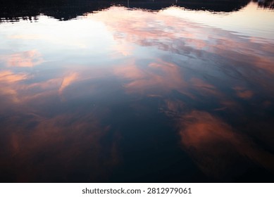 Abstract reflection of pink and blue sunset clouds mirrored across gently rippling harbor water.