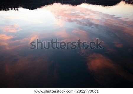 Abstract reflection of pink and blue sunset clouds mirrored across gently rippling harbor water.