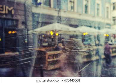 Abstract Reflection Summer Restaurant With Umbrellas And Yellow Lights Of The City In The Film On The Glass Building