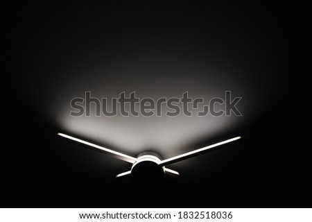 Abstract sconce lamp in shape of clock hands. Led lighting lamp closeup in darkness. Light and shadow abstraction 
