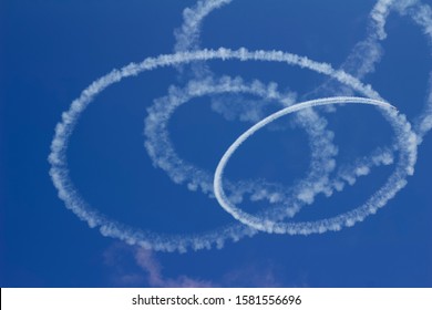 Abstract skywriting design with spiraling circles of vapor against a solid blue sky
