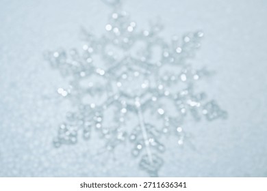 Abstract soft focus background featuring blurry silver snowflake ornament on a white surface, creating a dreamy bokeh effect, ideal for winter holiday or ethereal designs