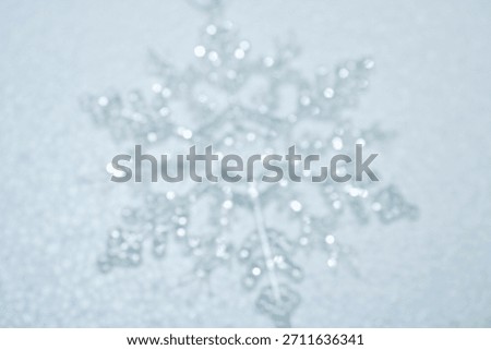 Abstract soft focus background featuring blurry silver snowflake ornament on a white surface, creating a dreamy bokeh effect, ideal for winter holiday or ethereal designs