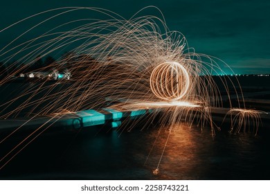 Abstract steel wool photography. The image is taken by setting steel wool on fire, spinning the fire and taking a long exposure photo at a jetty. while creating a ball of light, teal and orange. - Shutterstock ID 2258743221