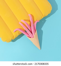 Abstract Summer Beach Layout Made Of Ice Cream Cone With Octopus Tentacles And Vibrant Yellow Travelling Air Pillow On Bright Blue Background. Minimal Vacation Concept. Trendy Sea Or Ocean Flat Lay.