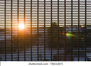 Abstract sunset shines through a metal screen at a train station.