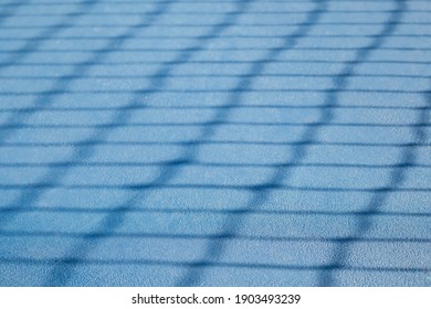 Abstract tennis court texture. Defocused tennis net shadow on ground, outside early morning. Blue rubberized and granulated ground surface for shock absorption. Tennis sport backdrop texture. - Powered by Shutterstock