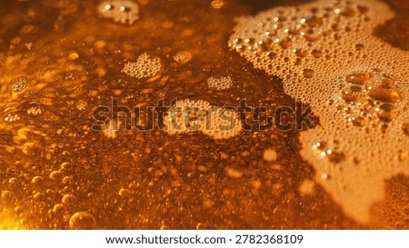 Abstract top view macro texture of golden oil with foam bubbles and sparkling reflections. Viscous liquid background for food, cosmetic or industrial concepts.