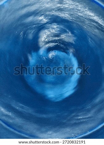 Abstract top view of a water vortex or whirlpool in a blue container, showing motion blur and circular texture