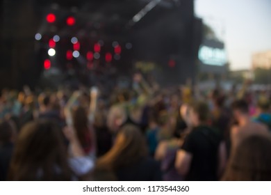 abstract unfocused blurred open air music festival and crowd of people near stage in evening bright sunset time with light glares