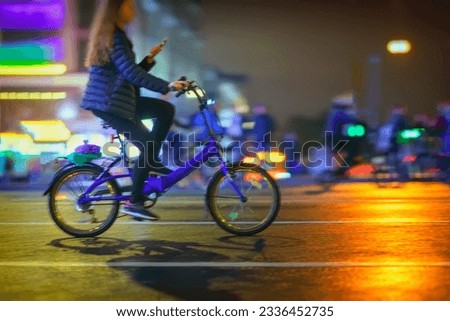 Abstract unrecognizable girl riding bike with smartphone, night city, illumination bokeh, motion blur. Healthy lifestyle, technology, leisure activity concept.