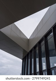 Abstract upward angle of clean, sharp geometric rooflines and dark glass windows of a modern commercial building under an overcast sky. The scene represents architectural minimalism, sharp lines, structural geometry, and contemporary corporate design.