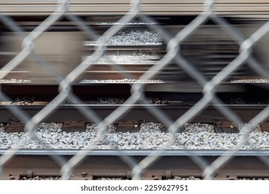 Abstract view of the bottom of a moving train on train tracks seen through an out of focus chain link fence