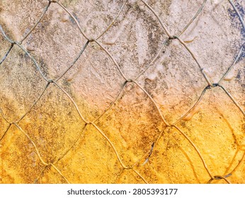Abstract view of a chain link wire fence against a weathered textured wall