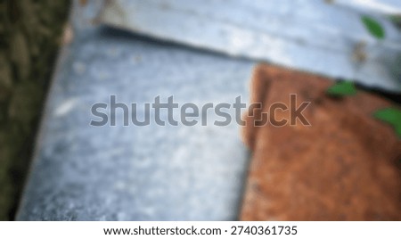 Abstract view contrasting rough galvanized metal texture next to an area showing deep reddish brown oxidation and small greenery.