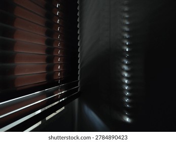 Abstract view of dramatic light rays streaming through closed venetian blinds in a dark interior. The strong perspective and shadow patterns on the wall create a moody, cinematic atmosphere. Perfect for concepts related to solitude, mystery, thriller, mental health, hope, or creativity. Commercial use with negative space for text and design.