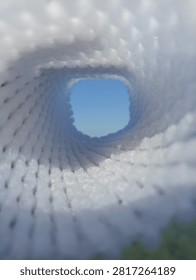 Abstract view looking through a white mesh tunnel towards the bright blue sky, light at the end of the tunnel concept