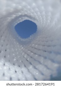 Abstract view looking through a white mesh tunnel towards the bright blue sky, light at the end of the tunnel concept