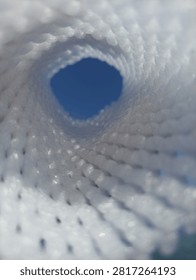 Abstract view looking through a white mesh tunnel towards the bright blue sky, light at the end of the tunnel concept