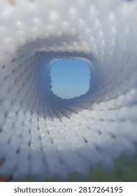 Abstract view looking through a white mesh tunnel towards the bright blue sky, light at the end of the tunnel concept
