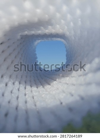 Abstract view looking through a white mesh tunnel towards the bright blue sky, light at the end of the tunnel concept