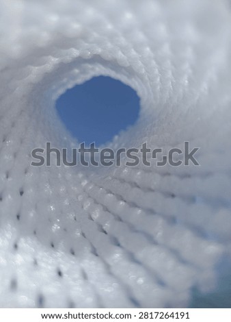 Abstract view looking through a white mesh tunnel towards the bright blue sky, light at the end of the tunnel concept