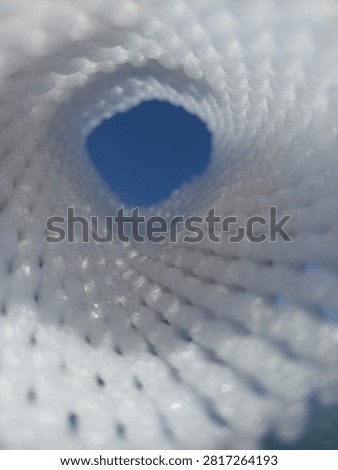 Abstract view looking through a white mesh tunnel towards the bright blue sky, light at the end of the tunnel concept