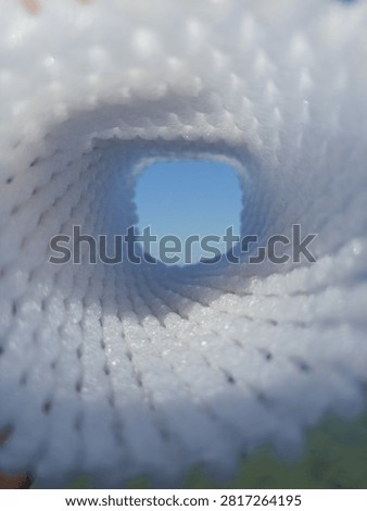 Abstract view looking through a white mesh tunnel towards the bright blue sky, light at the end of the tunnel concept