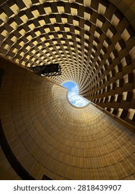 Abstract view looking upward inside a modern architectural structure with geometric curved ceiling and circular opening revealing blue sky. Contemporary architecture featuring repeating patterns, symmetry and futuristic design.