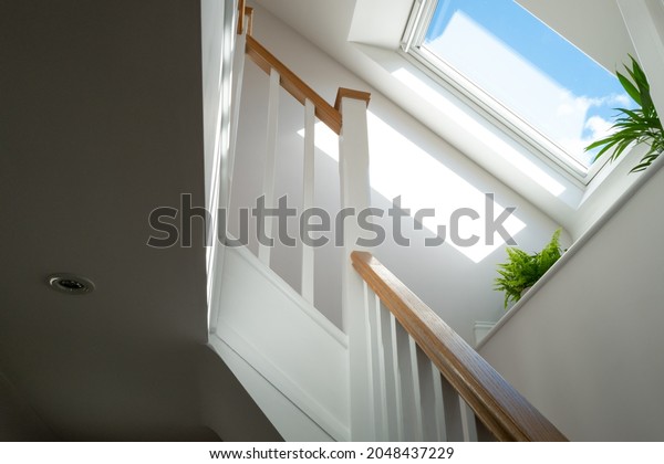 Abstract view of a newly installed loft\
conversion seen from the ground floor, looking at the staircase. A\
skylight window is seen on a sunny\
day.