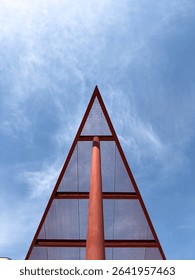 Abstract view of a red triangular metal structure with grid pattern, photographed from below against a bright blue sky, ideal for architecture and design inspiration.