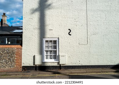 Abstract View Of A Telegraph Pole Shadow On An End Of Terraced House. The Shadow Follows Real Telephone Wires On The Blue Sky.