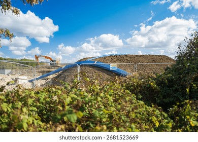 Abstract view, through a hedge of distant ground works being carried out for a new housing project in the UK. Top soil has recently been dumped on the site, as can be seen by the big mound.