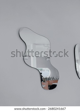 Abstract wall mirror with irregular shape reflecting minimalist interior and modern furniture, adding artistic and stylish decor element.