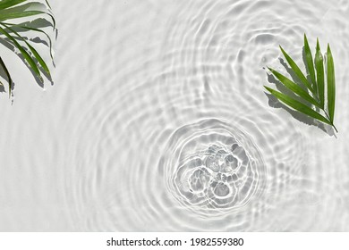 Abstract water texture, surface with drops, rings and ripple decorated palm leaves.Flat lay, top view, spa and wellness background with copy space