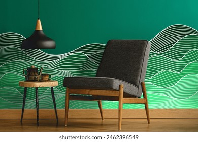 Abstract wave pattern wall decal or wall sticker on a teal green wall with a gray upholstered chair by a ceiling lamp over a wooden side table in a minimalist living room interior.