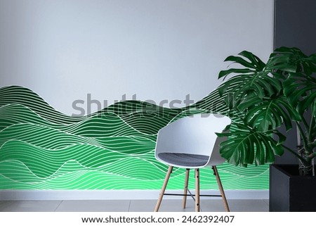 Abstract wave pattern wall decal or vinyl sticker in green shades on white wall with modern chair adjacent to planter.