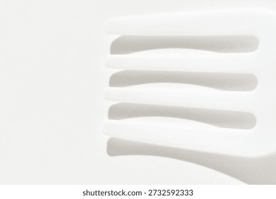 Abstract white plastic fork and shadows on bright smooth surface in minimalist composition.