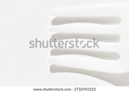 Abstract white plastic fork and shadows on bright smooth surface in minimalist composition.