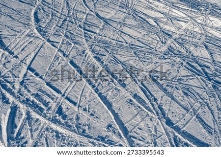 Abstract winter background featuring numerous crisscross ski tracks on a groomed mountain slope. High angle shot of snowy texture and sport activities pattern