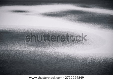 Abstract winter pattern of white snow forming an S-curve on the dark frozen surface of a lake
