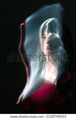 Abstract woman with red dress and black hairs silhouette in bright light trails of light painting. Portrait in the style of light painting. Long exposure photo. Image contains noise and motion blur